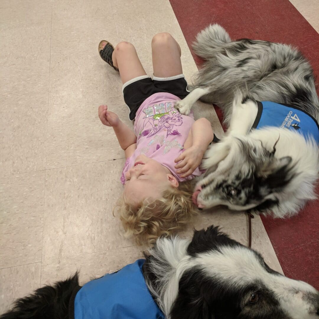 A little girl laying on the ground with two dogs.