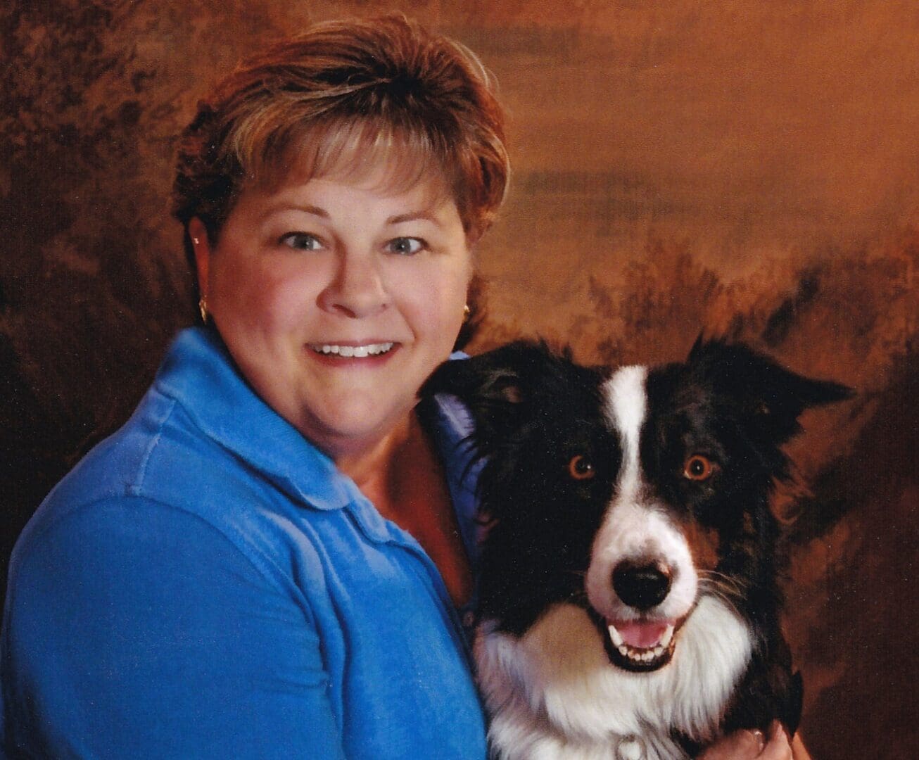 A woman holding her dog in front of a painting.